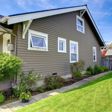 This beautiful Craftsman style house is made of shingle siding and features board and batten accents. It has a large front porch with columns and a gabled roof. The windows are framed with white trim and the door is painted a deep blue. The house has two stories and a large balcony on the second floor. It is the perfect place for a family to call home.