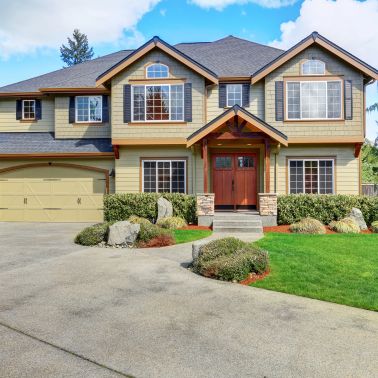 This medium-sized traditional house has a beige siding with shingles and a hip roof. The beige color of the siding is complemented by the dark brown of the hip roof creating a classic look. The house has a symmetrical design with two windows on either side of the front door and a chimney on the side. The overall look of the house is one of timeless elegance.